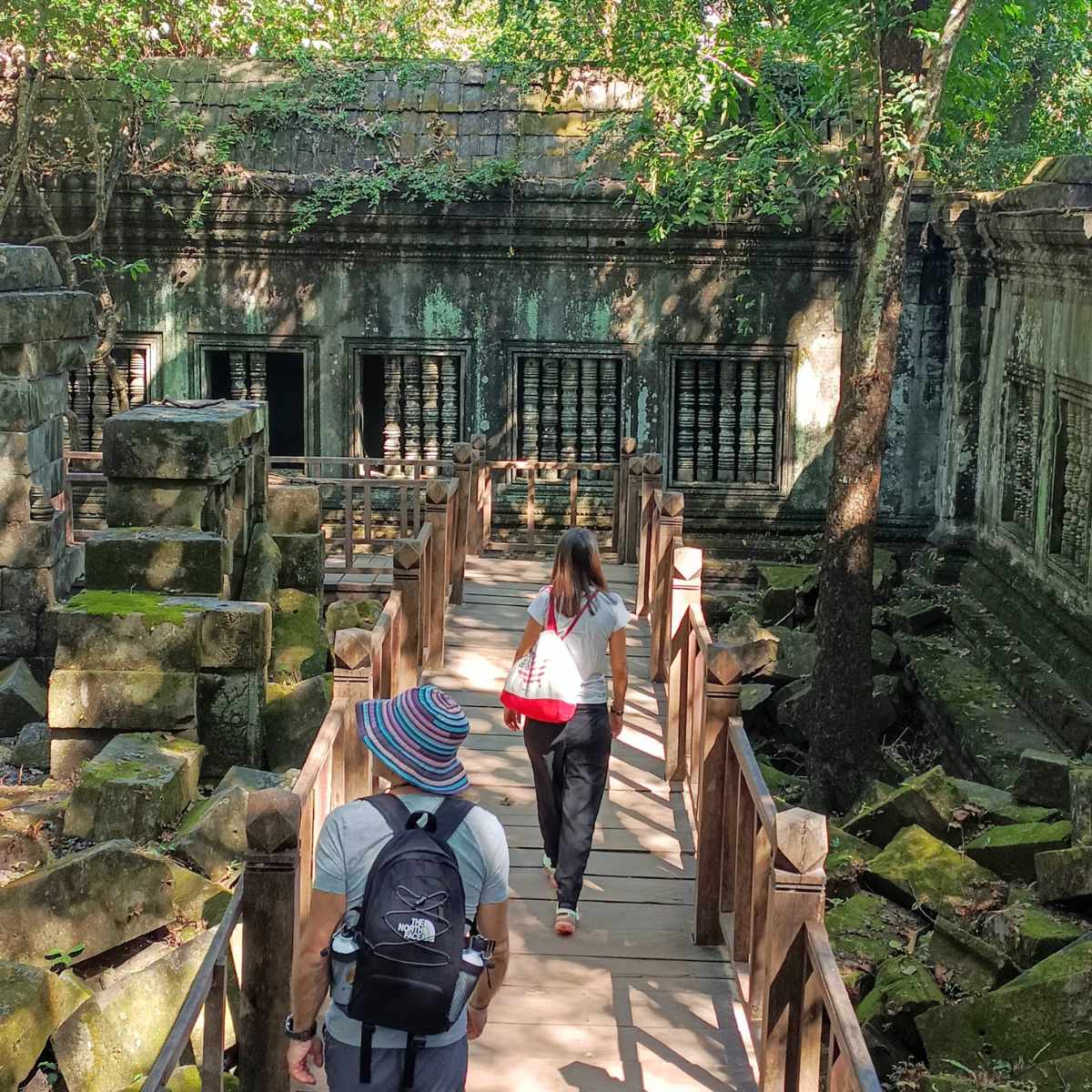 Beng Mealea and Floating Village Tour from Siem Reap with visitors walking on a wooden path through Beng Mealea temple ruins and shaded stone corridors